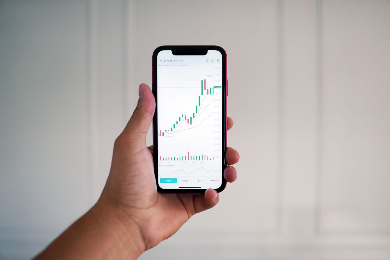 Vue rapprochée d’une main tenant un smartphone affichant un graphique boursier en intérieur.